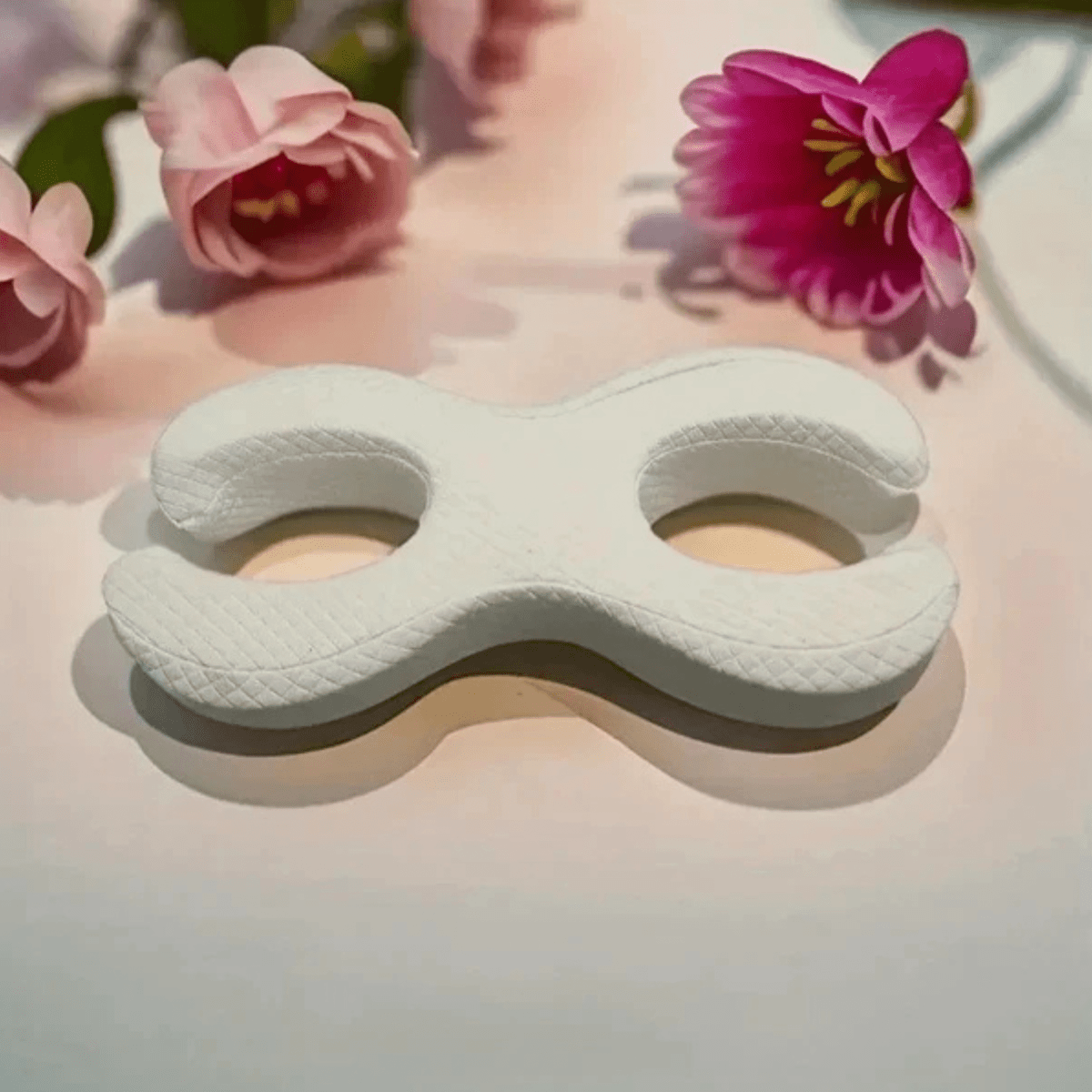 Anti-Aging Schlafkissen in weißer, ergonomischer Form, umgeben von Blumen für besseren Schlaf und glatte Haut.